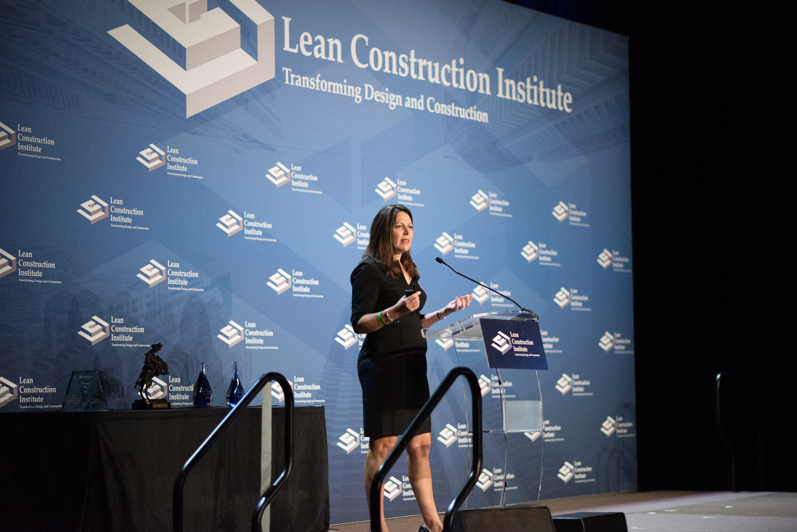 A woman provides a presentation about Lean services on a stage with the Lean Construction Institute logo in the backdrop