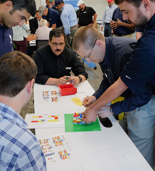 Several colleagues take part in the Parade of Trades Lean simulation at a work table using LEGOs.